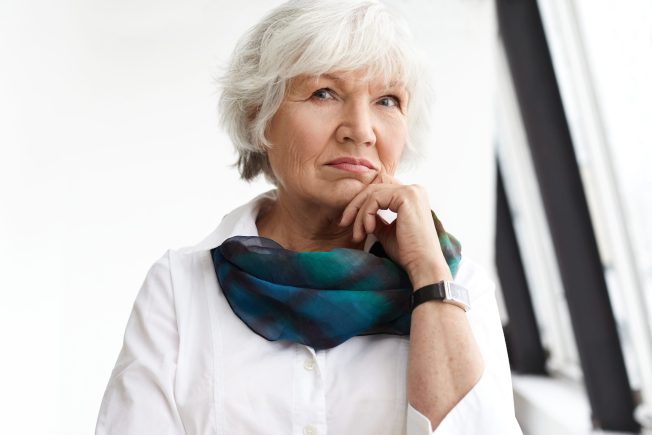 People, age, maturity and lifestyle concept. Portrait of stylish serious mature businesswoman with short white hair touching chin, having pensive look, thinking about business plans and ideas